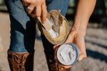 A person is applying a product to a horse's hoof using a wooden applicator paddle.