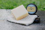 Bar of soap and container labeled 'Bee Pawsome' on a stone surface with grass in the background