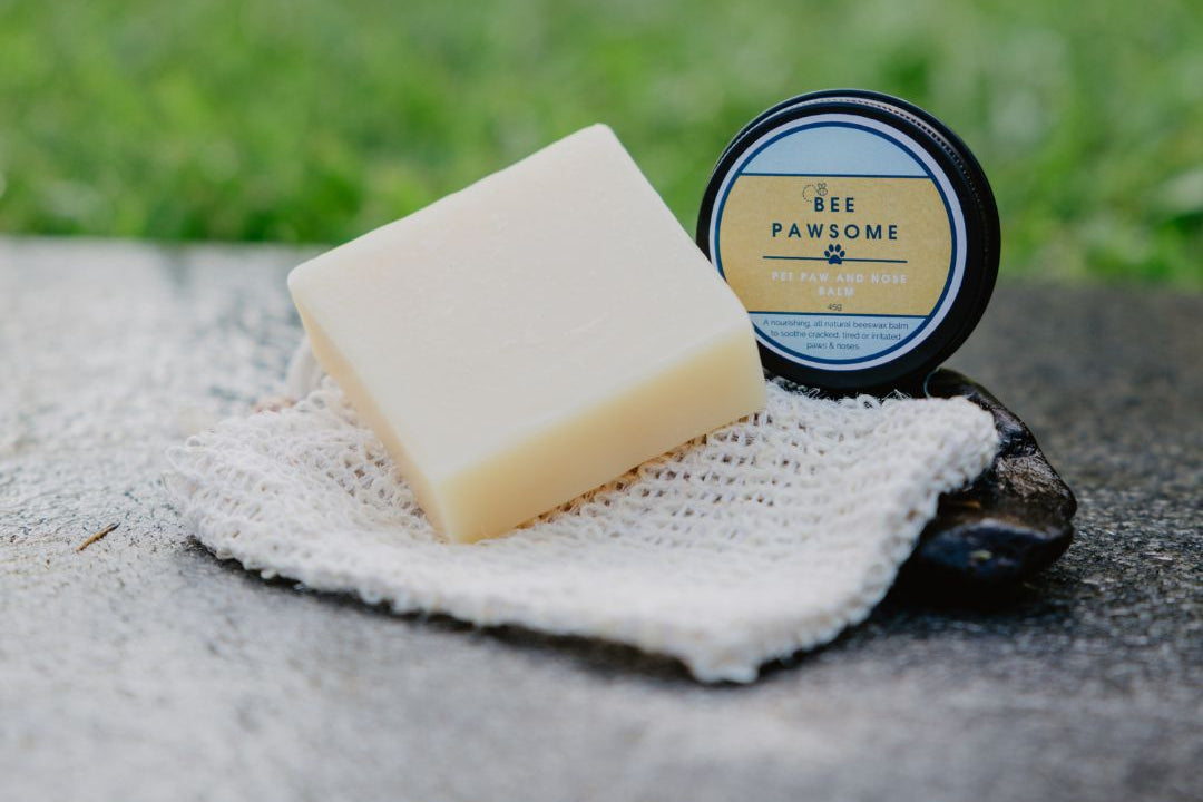Bar of soap and container labeled 'Bee Pawsome' on a stone surface with grass in the background