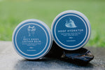 Two containers of 'Bee's Knees Leather Balm' and 'Hoof Hydrator' on a stone surface with a blurred green background.